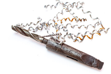 An industrial twist drill bit with a morse taper shank resting under long, spiraled metal shavings on a white background. © Александр Серебрянни