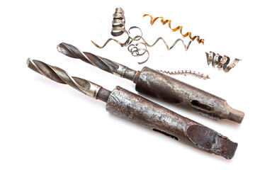 Two large industrial drill bits with morse taper shanks lying next to spiral metal shavings and swarf on a white background. © Александр Серебрянни
