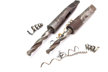 Two large industrial drill bits with morse taper shanks lying next to spiral metal shavings and swarf on a white background. © Александр Серебрянни
