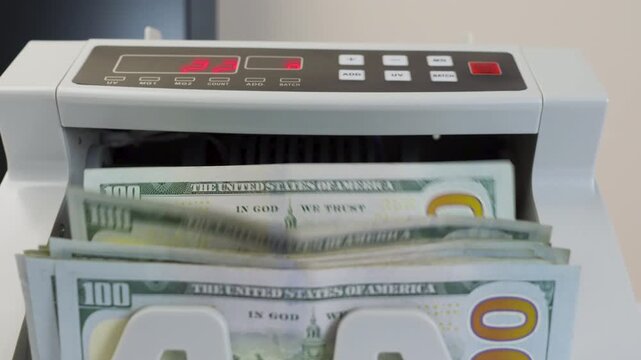 Money Counting Machine with Red Digital Display Processing a Stack of US 100 Dollar Bills 