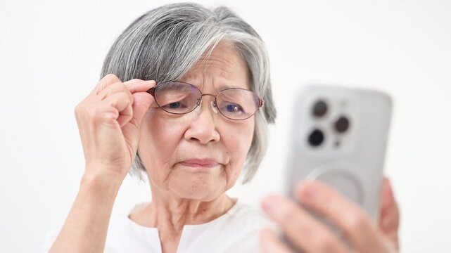 A gray-haired senior woman looking at her smartphone through reading glasses&mdash;a video where the text is hard to see