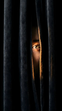 A single human eye peeking through dark velvet curtains with dramatic low light and shadows, conveying a sense of mystery and suspense.