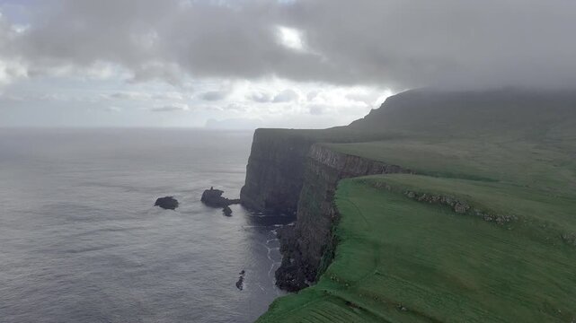 Dramatic landscape of steep coastal cliffs and green fields on a neighboring island near Mykines under stormy dark clouds, Faroe Islands - 어두운 먹구름 아래 펼쳐진 페로 제도 미키네스 주변 섬의 가파른 해안 절벽과 푸른 초원 대자연 풍경
