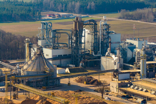 Aerial view of a wood processing factory with industrial machinery, silos, and piles of wood chips in a rural landscape in Poland.