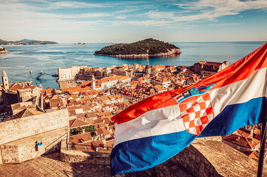 Aerial view of historic Dubrovnik with terracotta rooftops and the Croatian flag in the foreground, overlooking the Adriatic Sea, Dubrovnik, Dubrovnik-Neretva County, Croatia.