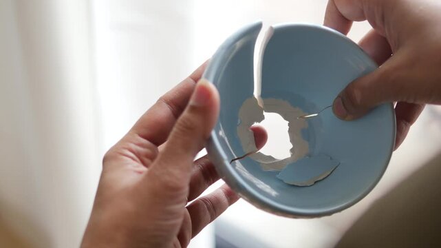 Hand holding broken blue bowl with cracks and hole