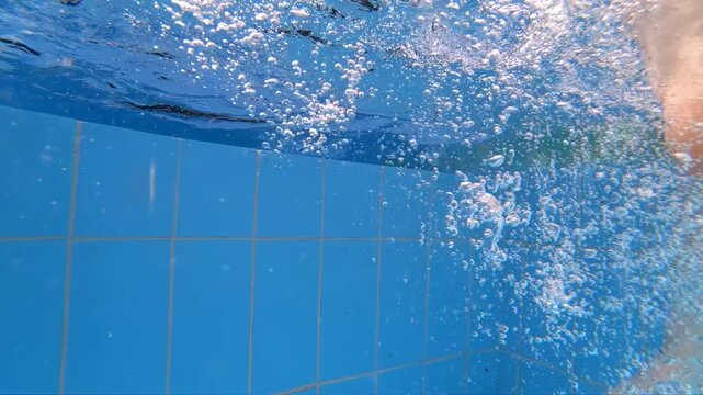 Slow motion underwater video of a girl dangles her feet in the pool water.