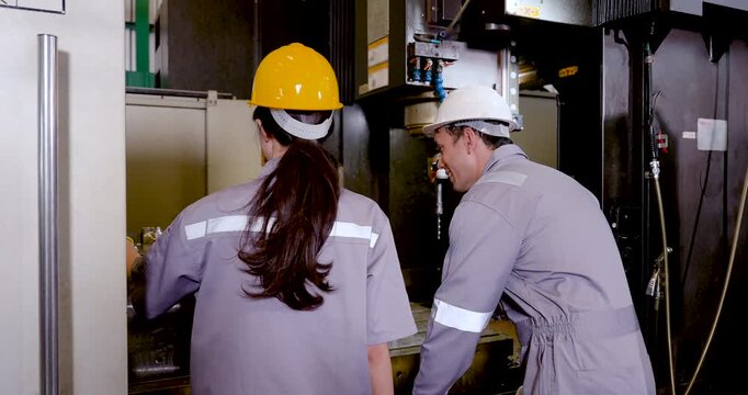 Asian woman technician and Asian man engineer move beside CNC machine, checking work area, verifying process step, and coordinating safe production supervision in workshop, slow motion