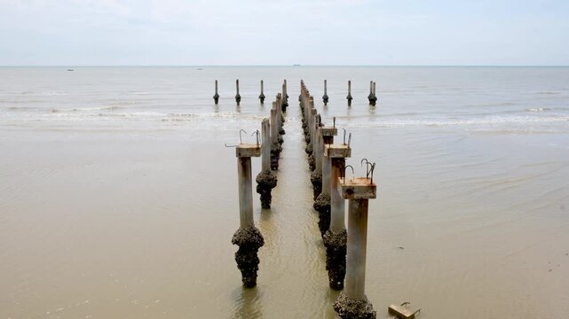 Abandoned concrete pillars of a ruined pier standing in the sea with gentle waves at Tanjung Lapin Beach, Rupat Island, Indonesia