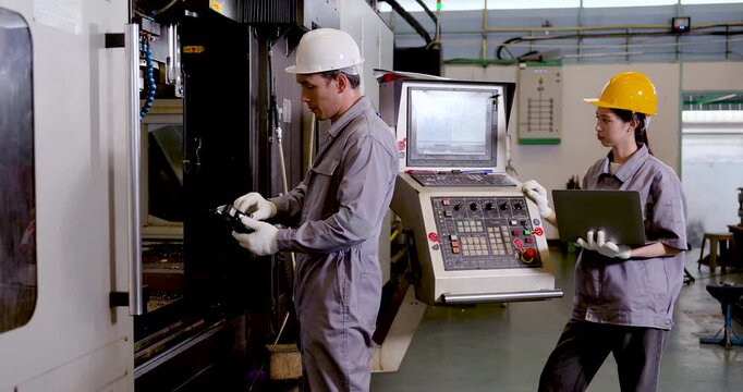 Asian man engineer handles machined component near CNC station while Asian woman technician monitors laptop, supporting inspection, data review, and safe production control in plant, slow motion