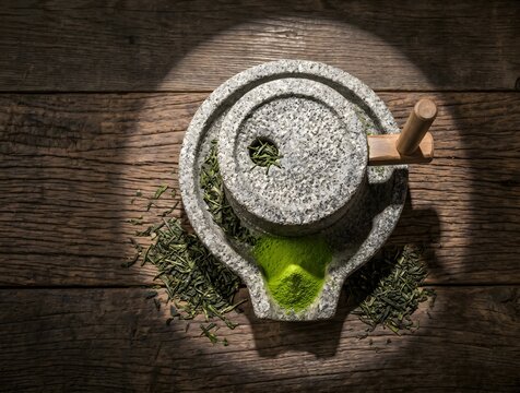 Top-down flat-lay of a traditional Japanese granite stone mill (ishi-usu) with a small precise cone of vibrant electric-green matcha powder formed at the lower spout.