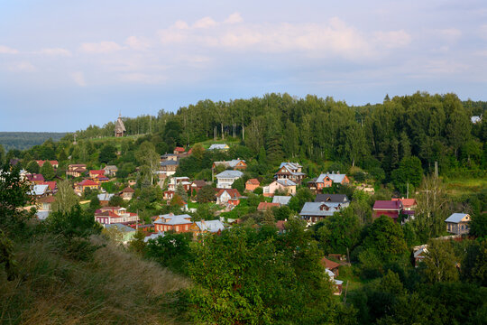 The town of Ples with traditional wooden houses in a hilly lowland covered with forest, with a wooden chapel on a hill, in the rays of sunset