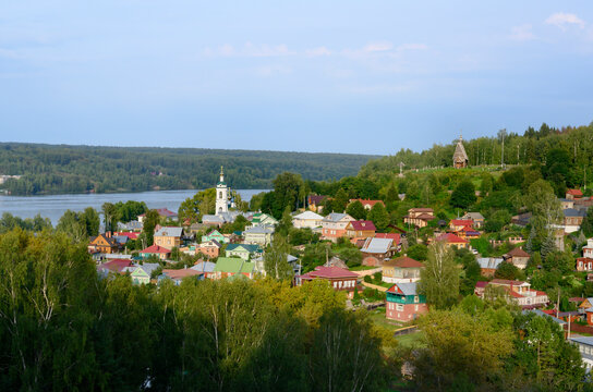 The town of Ples on the banks of the Volga River with wooden houses in a lowland covered with forest, with a church and a bell tower at sunset