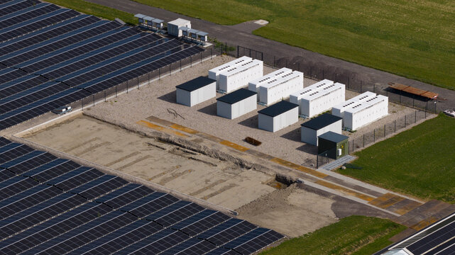 Aerial view of a solar farm featuring rows of photovoltaic panels and white battery energy storage system containers in Middenmeer, North Holland, Netherlands.