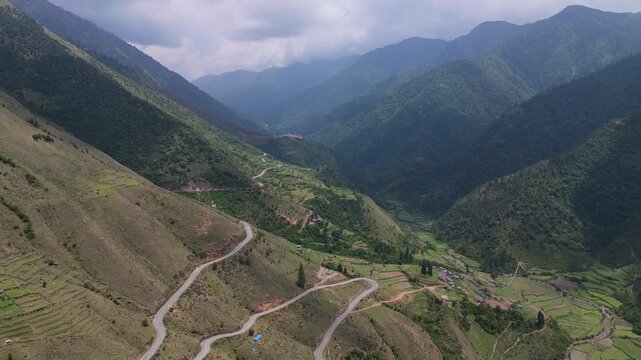 Title: Aerial view of winding mountain highway snaking through remote green valley, infrastructure and transportation engineering b-roll