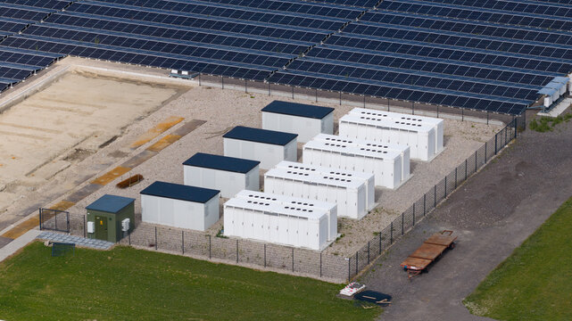 Aerial view of white battery energy storage system containers installed next to a large solar panel field in Middenmeer, North Holland, Netherlands.