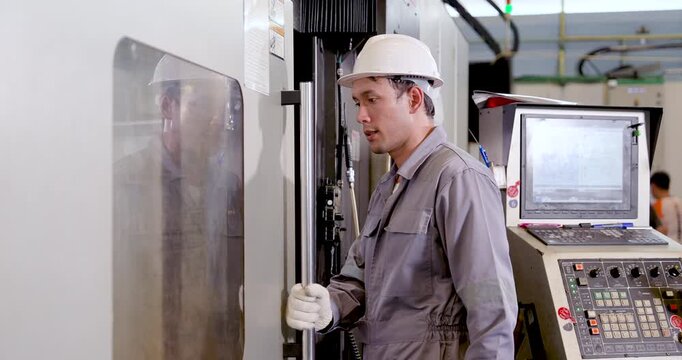 Asian technician opens CNC machine door and checks inner chamber before operation, reviewing tool area, safety status, machining readiness, production workflow, equipment condition in .