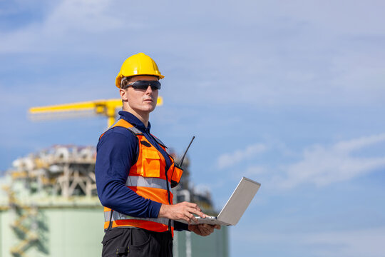 Engineer working on laptop at industrial site, Industrial worker in safety gear monitoring oil and gas terminal operations, Portrait of skilled engineer at industrial petrochemical and lng facility