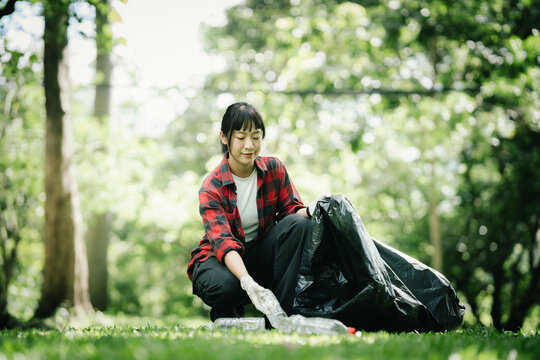 Young female volunteer collecting plastic bottles and litter in a public park, supporting environmental conservation, community cleanup, recycling efforts, and sustainable living.
