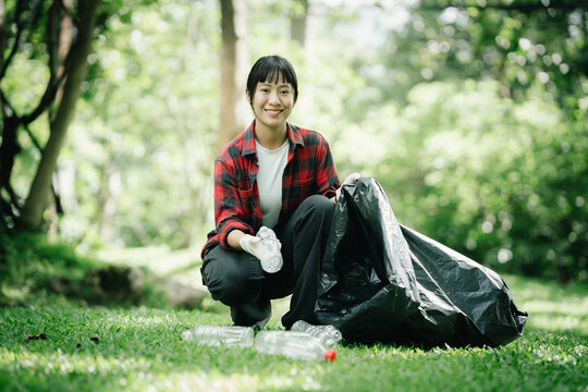 Young female volunteer collecting plastic bottles and litter in a public park, supporting environmental conservation, community cleanup, recycling efforts, and sustainable living.