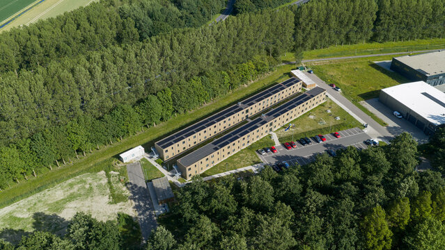 Aerial view of a modern residential complex with solar panels on the roofs, surrounded by lush green trees and a parking area in Middenmeer, North Holland, Netherlands.