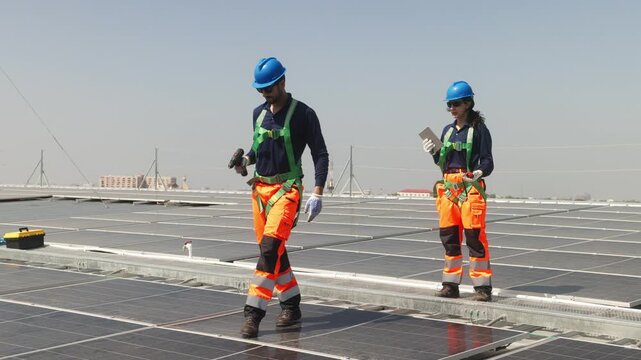 Two solar technicians inspecting rooftop photovoltaic panels, one adjusting panel alignment while colleague points and checks installation details.