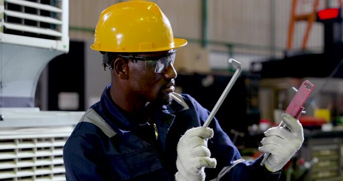 African technician in hardhat and glove holds wrench and screwdriver, preparing maintenance task and equipment check for safe industrial repair workflow in manufacturing plant, slow motion task