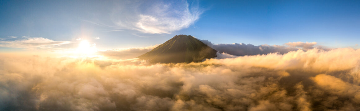 Aerial view of a mountain peak rising above a dense sea of clouds during golden hour in Adipuro, Jawa Tengah, Indonesia.