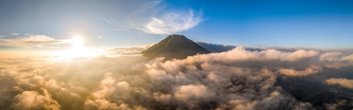 Aerial view of a majestic volcano peak rising above a dense sea of clouds during a golden sunrise in Adipuro, Jawa Tengah, Indonesia.