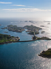 Fototapeta premium Aerial view of Lofoten near Svolvaer and Henningsvaer, Norway shows rocky islets, turquoise channels, a curving causeway and bridge, small harbors, and clustered buildings on a bright day.