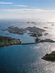 Aerial view of Lofoten near Svolvaer and Henningsvaer, Norway shows rocky islets, turquoise channels, a curving causeway and bridge, small harbors, and clustered buildings on a bright day. © Aerial Film Studio