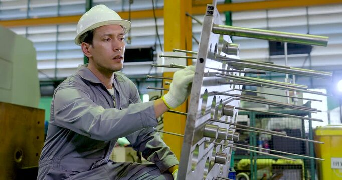 Asian technician adjusts metal guide rod on fixture frame, checking alignment, component spacing, safety step, precision manufacturing setup, maintenance workflow in , slow motion.