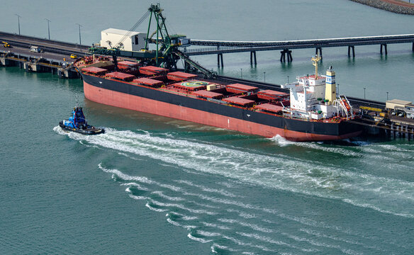 Tug boat passing by a coat ship and creating wash lines in the water in Port Curtis