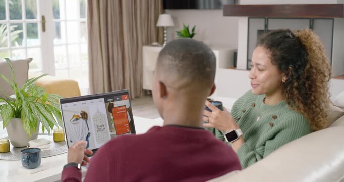 Diverse couple on sofa browsing promo urging man pointing clicking laptop woman holding cup smiling