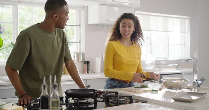 Diverse couple sharing glance at island, man lighting stove and cooking, woman snipping with shears