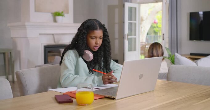 African American mother and teen daughter, teen writing using orange pencil in laptop class at home
