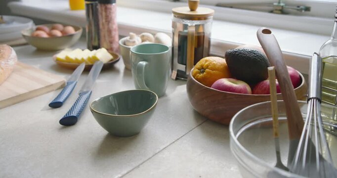 Camera is sliding left, revealing glass bowl with whisk, spatula on sunlit counter breakfast prep