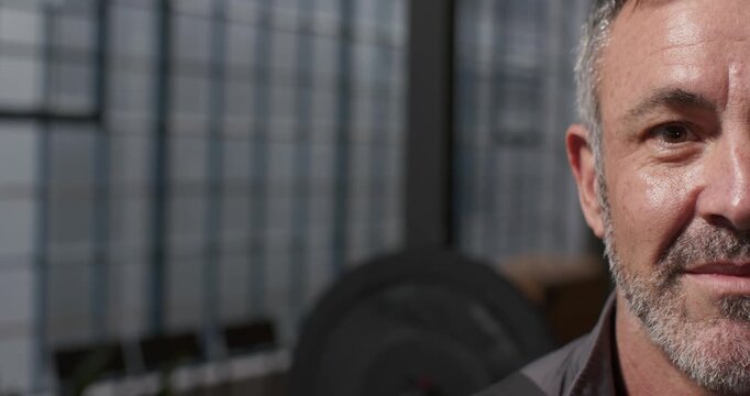 Middle-aged man in dark collared shirt smiling and laughing in gym by weight plate, copy space