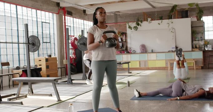 Diverse gym class, African American woman on cue doing goblet squat, hinging kettlebell for toning