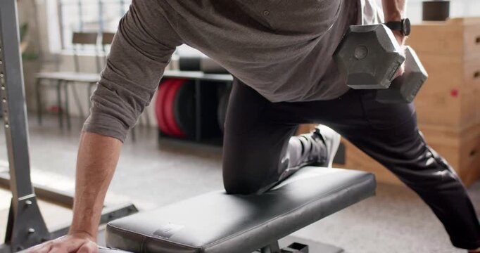 Adult male is bracing hand on bench, shifting stance, and pulling dumbbell upward for back strength