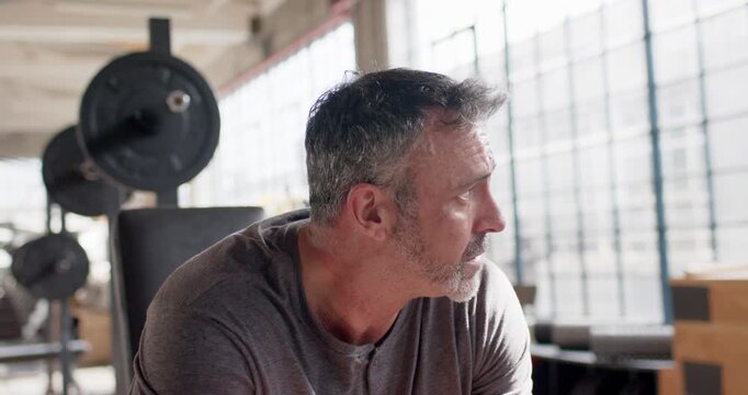 Middle-aged man sitting on bench by barbell in gym loft, hearing off-camera cue, turning to camera