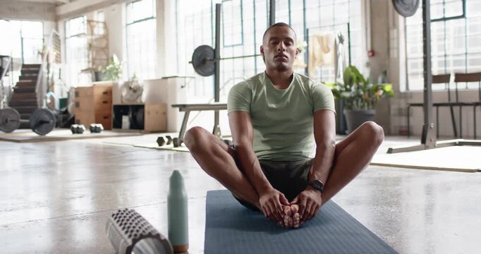 Man wearing light green shirt sitting on blue mat holding butterfly stretch, preparing for workout