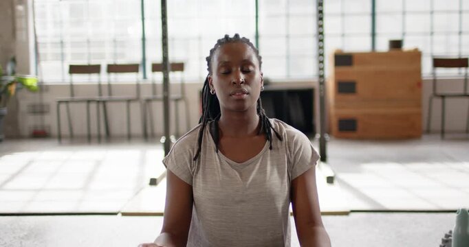 African American woman sitting on mat in lit studio, finishing meditation and opening eyes, smiling