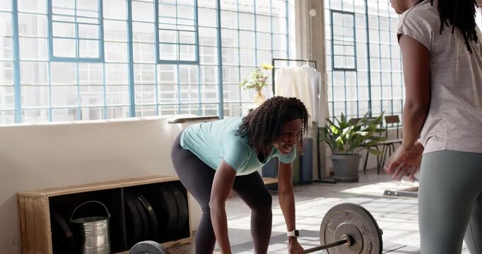 African female coach and trainee at gym clapping as turquoise tee breathing, pressing barbell work