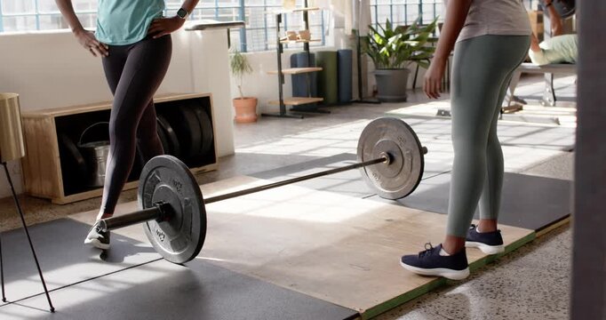 African American women in sportswear preparing lift in gym, grabbing chalk and coaching for barbell