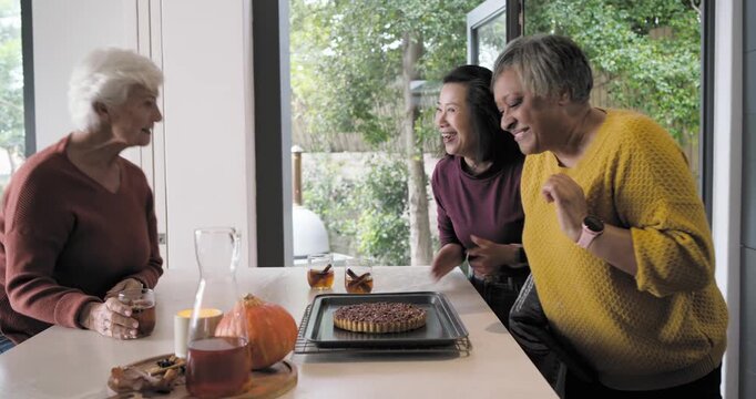 Diverse female friends inspecting tart after oven mitts removal at kitchen table, checking aroma