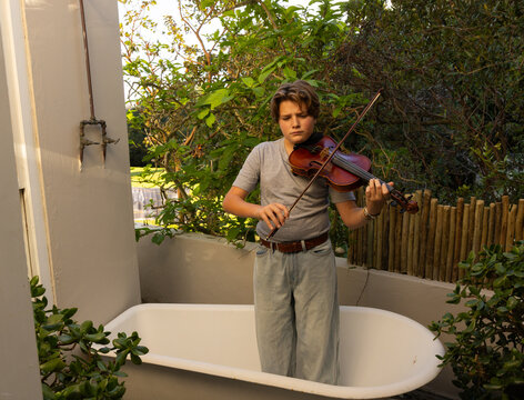 classic portrait of pre teen boy playing violin in outdoor tub
