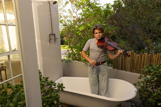 classic portrait of pre teen boy playing violin in outdoor tub