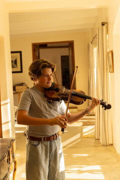 pre teen boy playing violin indoors at sunset