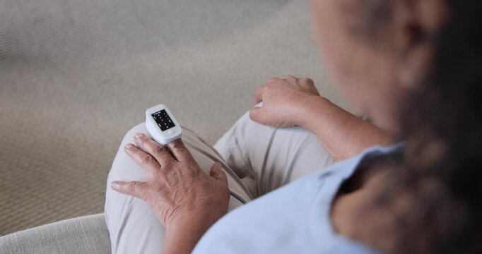 Senior African American woman seeing pulse oximeter lighting, adjusting to read on sofa, copy space